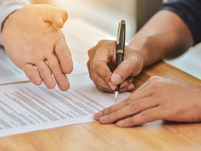 due mani una tiene in mano una penna, firma un foglio